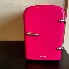 a bright pink refrigerator sitting on top of a wooden table next to a white wall