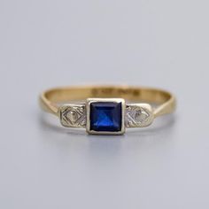 Solid 9K Gold Art Deco Diamond Ring A 9K gold Art Deco ring featuring a square-cut sapphire as its centrepiece. The sapphire's deep blue color is highlighted by its precise, geometric cut, which is characteristic of the Art Deco period. The ring's shoulders are decorated with intricate platinum patterns, including geometric motifs typical of the Art Deco style. Vintage piece in good condition, see images for more detail. Size - M+ Stone Diameter - 4.5 mm Weight - 1.5g 9ct gold ✅ Domestic and int Modern Blue Sapphire Ring In 14k Gold, Art Deco Blue Asscher Cut Ring, Modern Blue Sapphire Ring Hallmarked, Blue Sapphire Ring With Diamond Cut Asscher Shape, Formal Rectangular Sapphire Ring Fine Jewelry, Blue Asscher Cut Diamond Sapphire Ring, Square Cut Sapphire Ring For Formal Occasions, Blue Asscher Cut Sapphire Ring With Diamond Cut, Blue Asscher Cut Sapphire Ring With Diamond Details