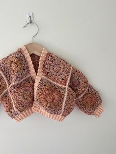 a knitted sweater hanging on a hook with clothes pins attached to the hanger