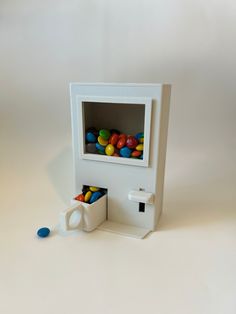 a white toy machine with balls in it's compartment and a blue plastic cup next to it