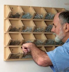 a man is looking at screws in a wooden storage box on the wall behind him