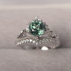 an engagement ring with a green stone surrounded by white diamonds on a gray background,