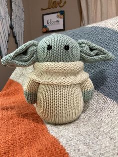 a knitted baby yoda doll sitting on top of an orange and white blanket