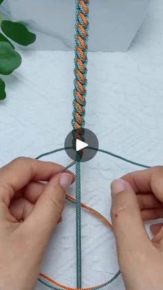 two hands are holding an orange and green rope