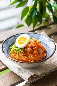 a bowl filled with noodles, meat and an egg on top of it next to a potted plant