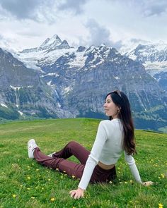 a woman sitting on the grass in front of mountains