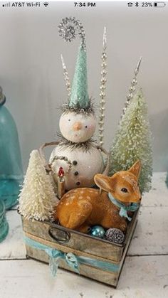 a wooden box filled with christmas decorations on top of a white table next to blue glass bottles