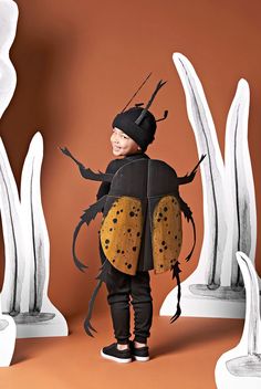 a little boy dressed up as a bug in front of some white and brown sculptures