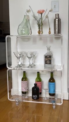 a shelf with bottles and glasses on it in the middle of a wooden floored room