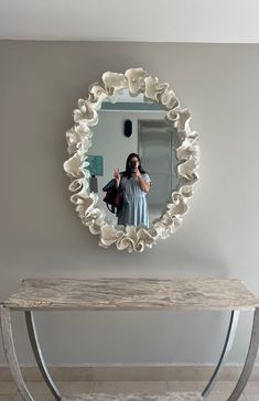 a woman taking a selfie in front of a round mirror on a wall above a bench