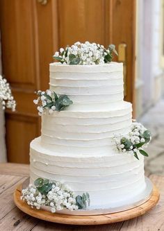 a wedding cake with white frosting and greenery on top is sitting on a wooden table