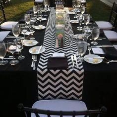 a long table is set up with black and white napkins, silverware, and wine glasses