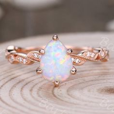 an opal and diamond ring sitting on top of a piece of wood with white diamonds