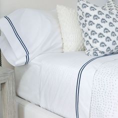 a bed with white sheets and blue trimmings on the headboard is shown