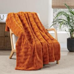 an orange blanket sitting on top of a wooden chair next to a potted plant