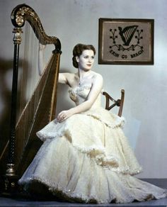 a woman in a white dress sitting on a chair next to a large wooden harp