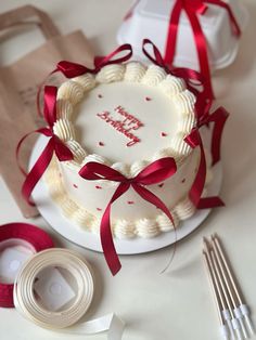 a white cake with red ribbon on it sitting next to some silverware and napkins