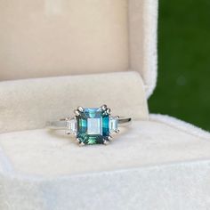 an engagement ring with blue and white stones in a box on top of the grass