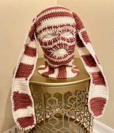 a red and white knitted hat sitting on top of a metal stand next to a wall