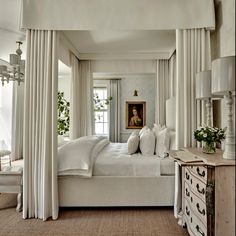 a bedroom with white bedding and drapes hanging from the ceiling, along with a painting on the wall