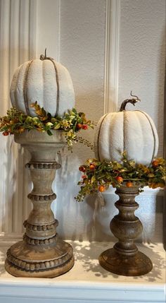 two white pumpkins sitting on top of a shelf next to each other in vases