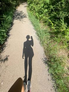 the shadow of a person standing on a dirt road in front of bushes and trees