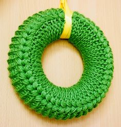 a green crocheted wreath hanging on a wooden table with a yellow ribbon around it