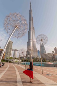 a woman is standing in front of the burj building and looking at the ferris wheel