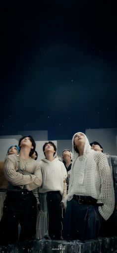 four people are standing in front of a black background and one is looking up at the sky