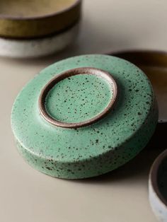 three ceramic bowls and one with a ring on it sitting next to each other in different colors