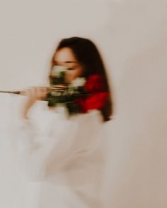 a woman in white dress holding a flower and aiming it at the camera with both hands