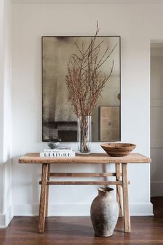 a wooden table topped with a vase filled with flowers next to a painting on the wall