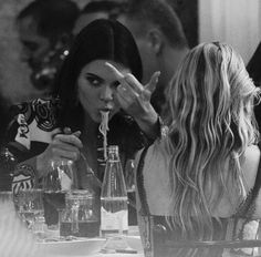 two women sitting at a table with drinks in their hands and one woman holding her face up to her mouth