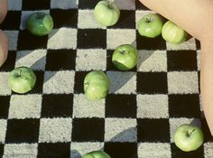 several green apples sitting on top of a black and white checkered rug