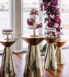 three cakes sitting on top of gold pedestals in front of a window filled with flowers