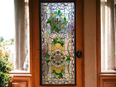 a stained glass front door with flowers and leaves on the window sill, next to a potted plant