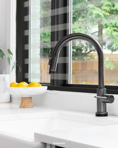 a kitchen sink with a bowl of lemons on the counter and a window in the background