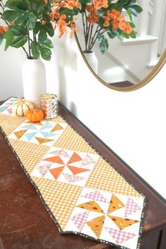 an orange and white table runner sitting on top of a wooden table next to a potted plant