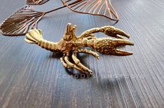 a gold crab brooch sitting on top of a wooden table next to other metal items