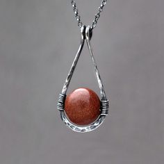 Goldstone Teardrop Necklace. Hammered Sterling Silver pendant. Autumnal terracotta brown / red gemstone jewellery. Created using beautiful Goldstone coin bead wire wrapped to a hammered hand forged sterling silver teardrop frame. Goldstone is a beautiful sparkly man-made `stone`; it is said that it was accidentally discovered by Italian monks practicing alchemy who split molten copper into molten glass. Metal particles are suspended within glass to give goldstone its striking twinkle, copper is used in the brown-red version of goldstone. Finished with a delicate sterling silver rolo style chain, adjustable in lenght and a lobster clasp. The frame has been hammered and hand polished for more strength and character. Available in bright or oxidized (darkened) sterling silver.  DETAILS  Stone Brown Teardrop Jewelry For Gift, Brown Gemstone Copper Jewelry, Brown Copper Jewelry With Gemstone, Brown Copper Gemstone Jewelry, Red Gemstone Drop Jewelry, Artisan Teardrop Gemstone Beads Jewelry, Red Drop Gemstone Jewelry, Red Teardrop Gemstone Drop Necklace, Copper Teardrop Necklace For Gifts