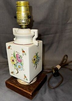 a white vase with flowers on it sitting on top of a wooden stand next to a cord