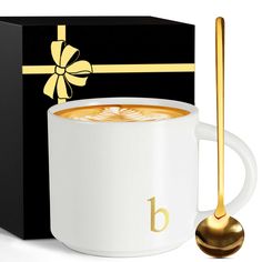 a white coffee cup with a gold spoon in front of it and a black box