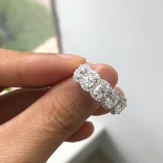 a woman's hand holding an engagement ring in front of a window sill