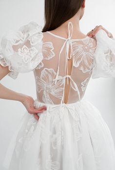 the back of a woman wearing a white dress with floral appliques on it