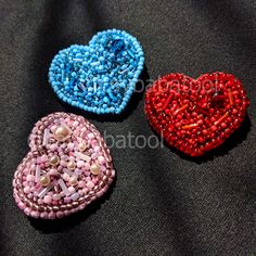 three heart shaped beaded brooches on a black surface