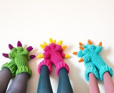 four crocheted dragon mittens are lined up in a row on a white surface