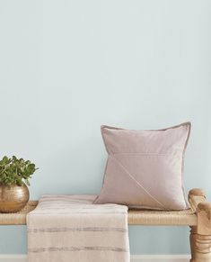 a wooden bench topped with a pillow next to a potted plant and a blanket