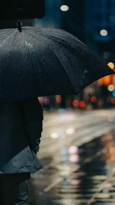 a person standing in the rain holding an umbrella over their head and looking at the street