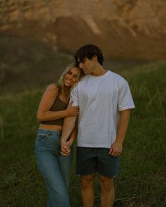 a young man and woman standing together in the grass with their arms around each other