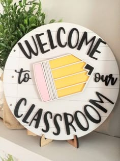 welcome to our classroom sign on a shelf with potted plant in the corner behind it